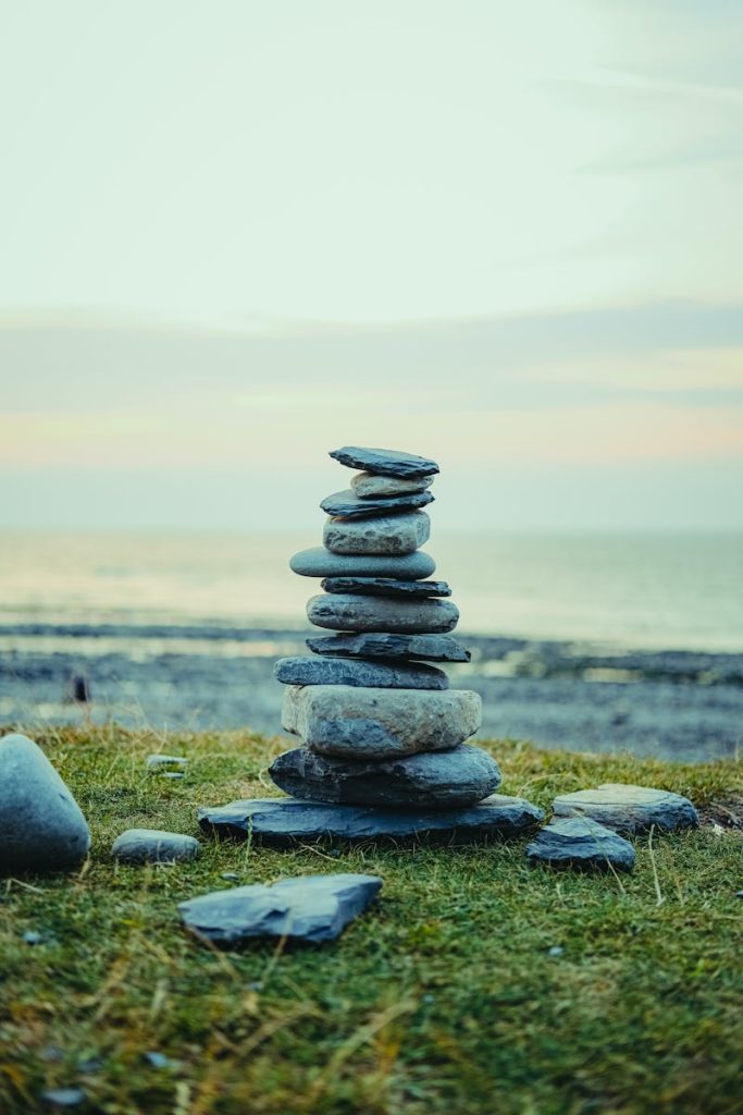 Serene beach scene featuring a cairn of stacked stones on grass with a calming sunset backdrop.